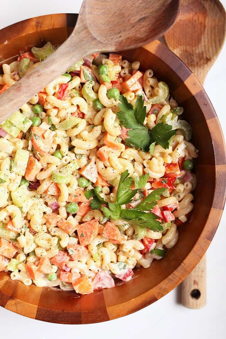 vegan macaroni salad in a wooden bowl with two wooden spoons on a white countertop 