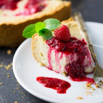 a slice of vegan cheesecake with raspberry sauce on a white plate