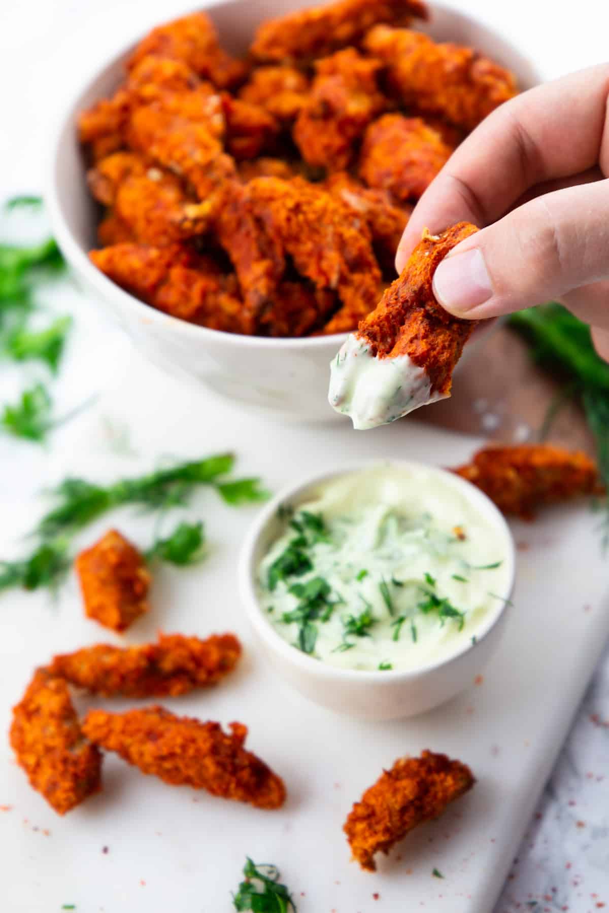 a hand dipping a vegan chicken finger into a small bowl of ranch sauce 