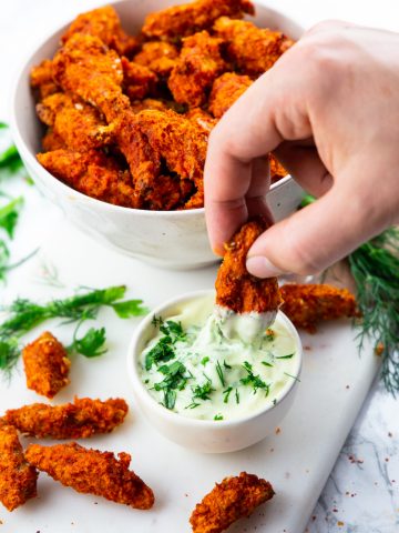 a hand dipping a vegan chicken finger into a small bowl of mayonnaise