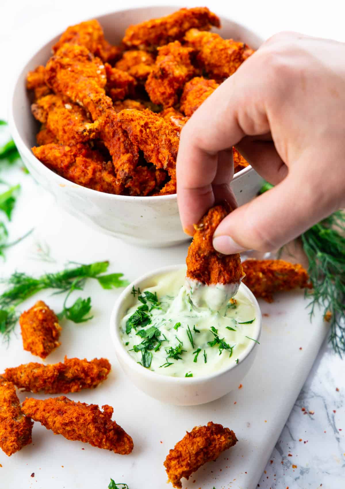a hand dipping a vegan chicken finger into a small bowl of mayonnaise 
