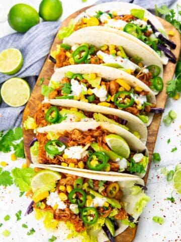 six jackfruit tacos on a wooden cutting board with limes on the side