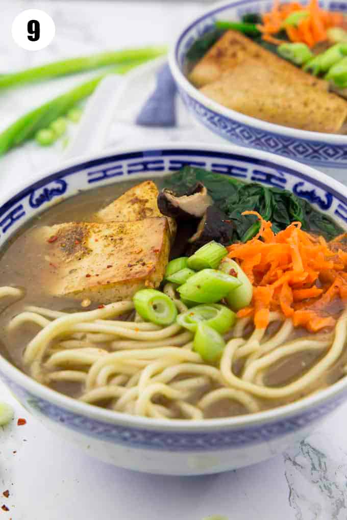 a bowl with ramen with tofu, carrots, and spinach on a marble countertop 