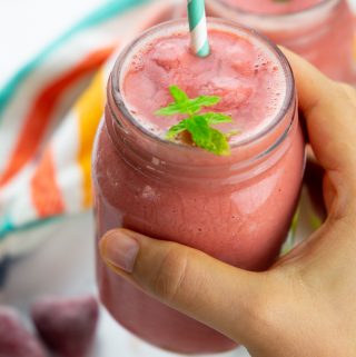 a hand holding a watermelon smoothie with a straw and fresh mint on top