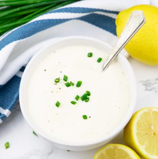 a white bowl with sour cream with lemons and chives on the side