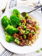 teriyaki tofu with brown rice and broccoli in a white bowl with a fork