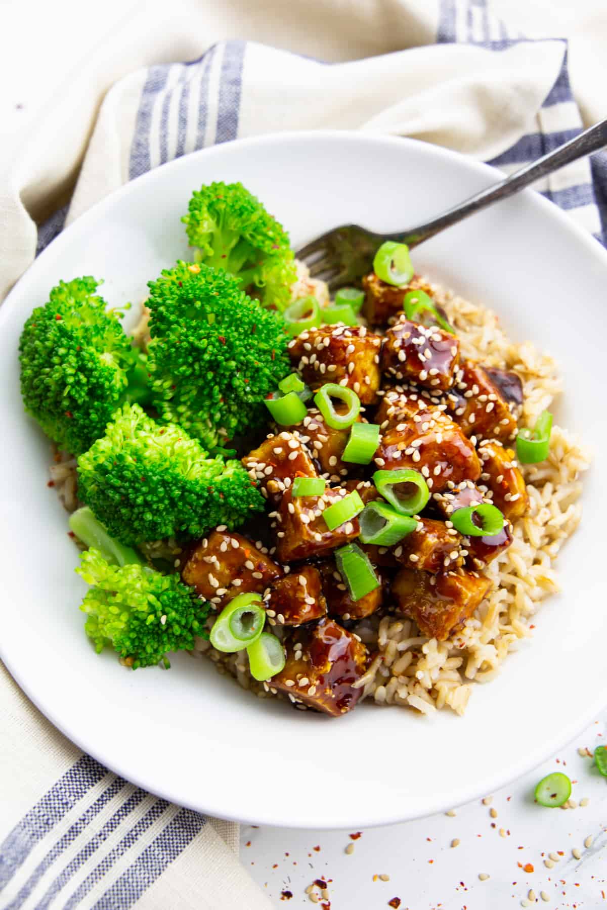 teriyaki tofu with brown rice and broccoli in a white bowl with a fork