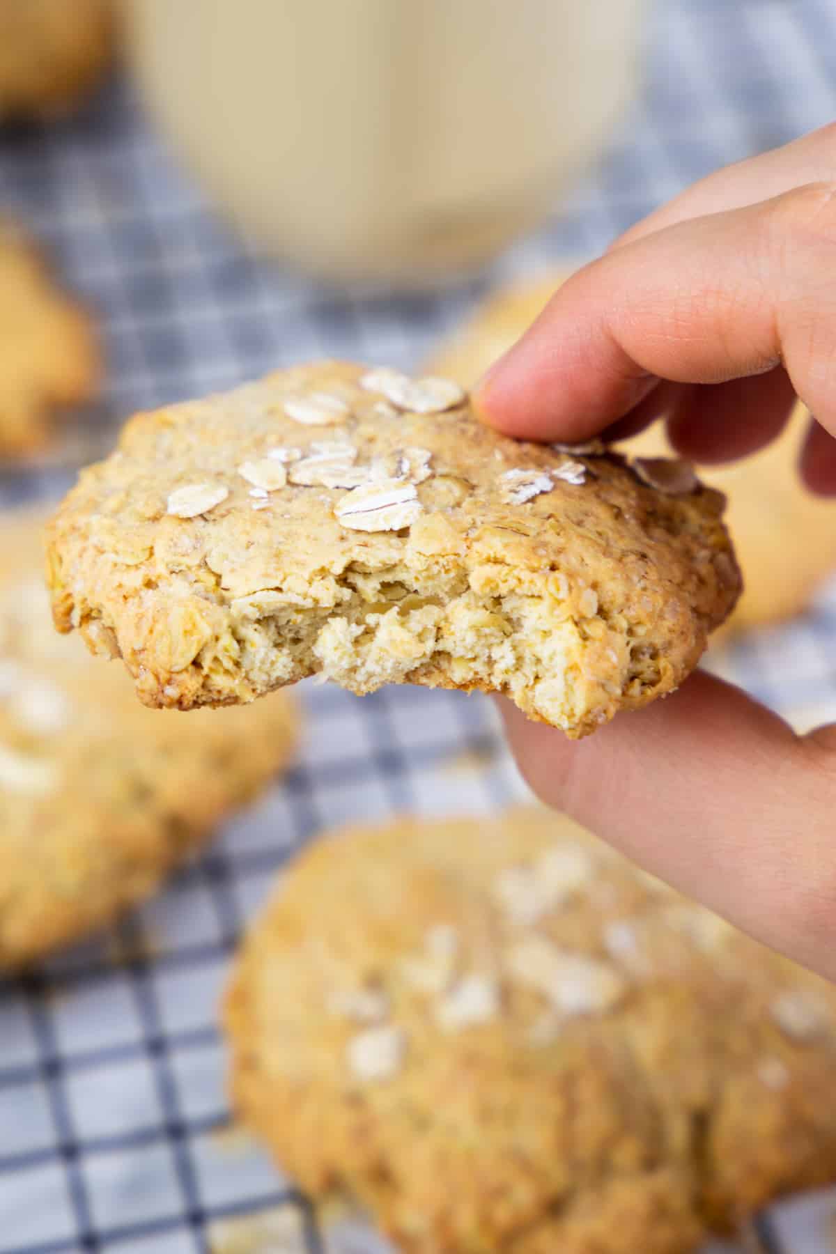 a hand holding an oatmeal cookie over a cooling rack with more cookies 