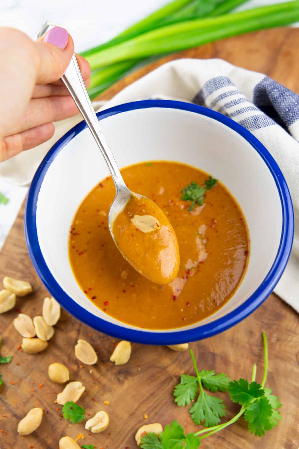 a hand dipping a spoon into a bowl of peanut sauce 