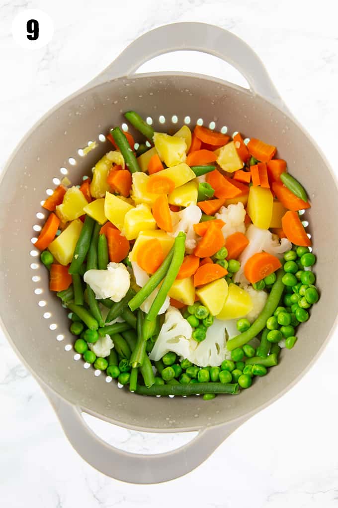 cooked potatoes, carrots, beans, cauliflower, and peas in a colander 