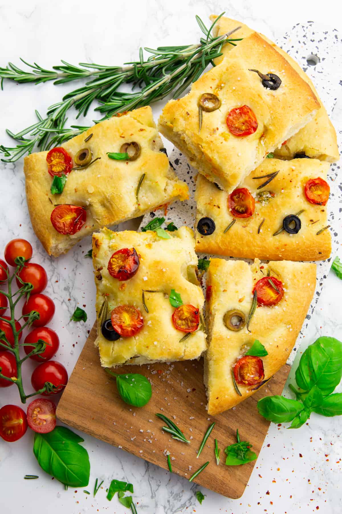 Focaccia squares on a wooden board with cherry tomatoes, rosemary, and basil on the side