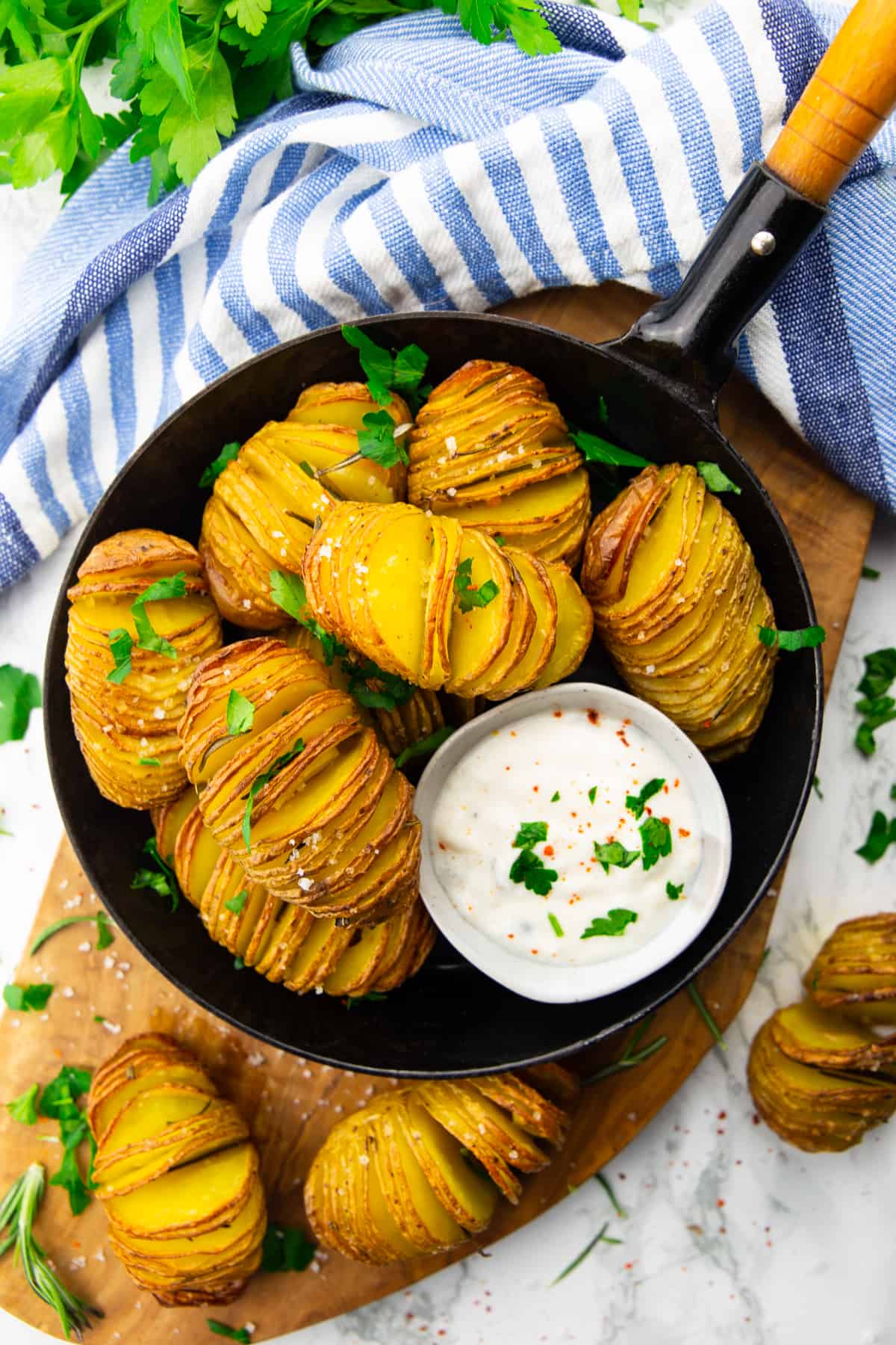 hasselback potatoes in a black pan on a wooden board with a small bowl of sour cream on the side