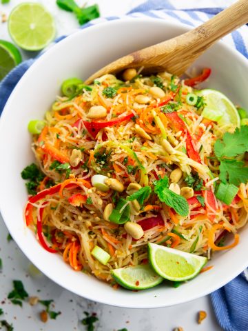 a bowl with noodle salad with spiralized vegetables and lime wedges on a marble countertop