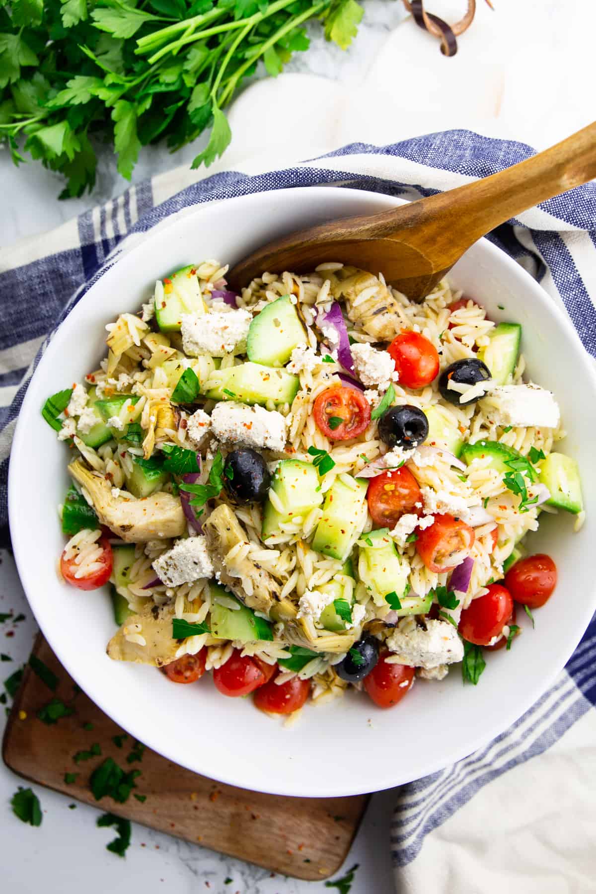 orzo pasta salad in a white bowl with a wooden spoon on a marble countertop 