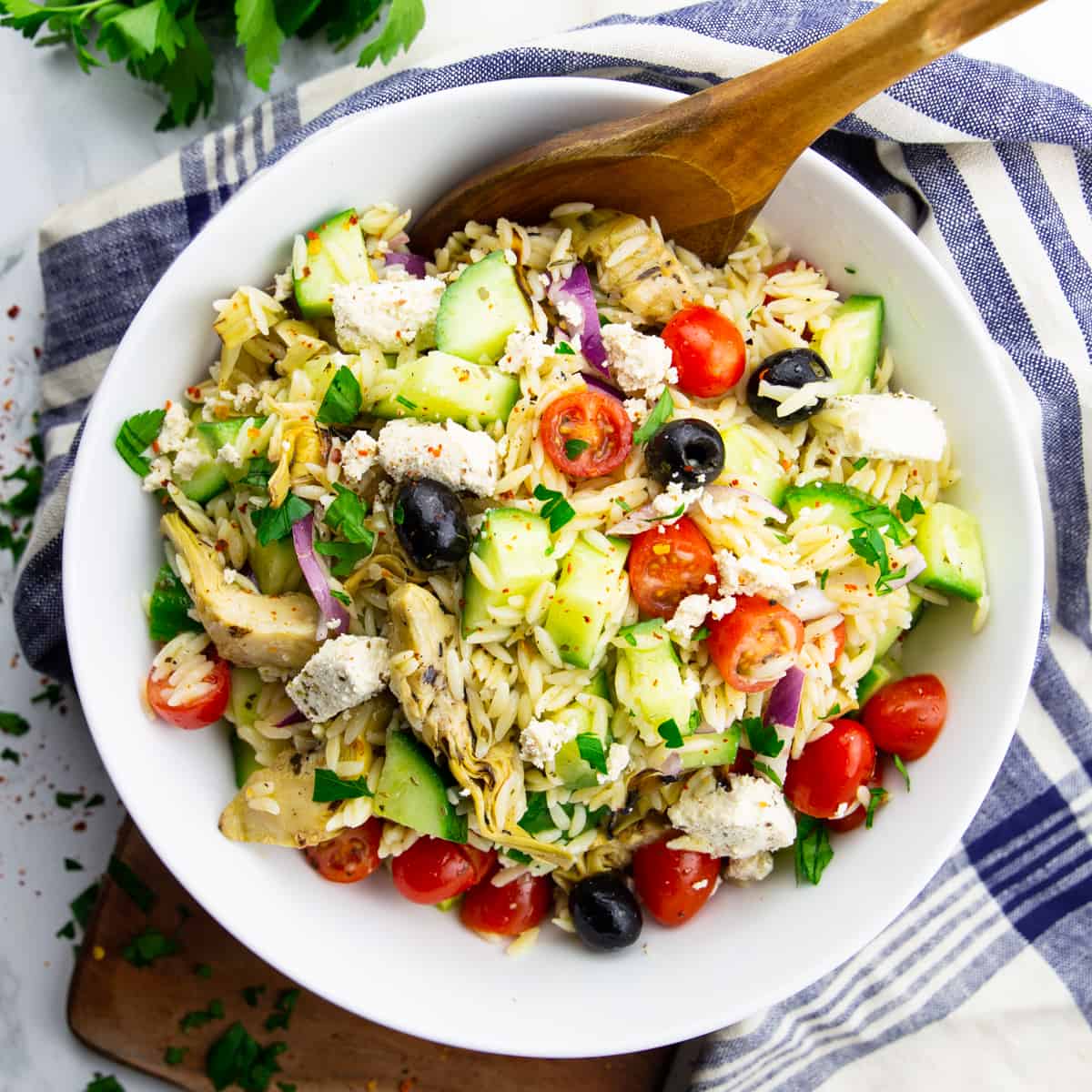 orzo pasta salad in a white bowl with a wooden spoon on a marble countertop