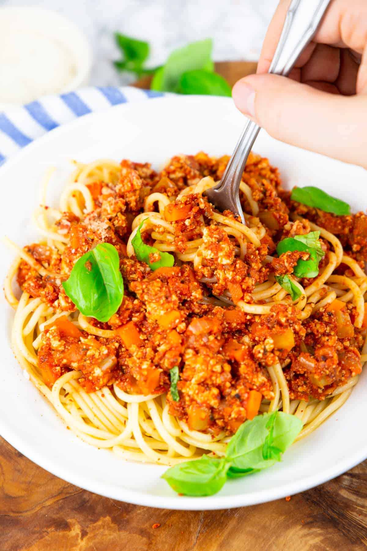 a hand with a fork picking up spaghetti with vegan bolognese out of a white bowl