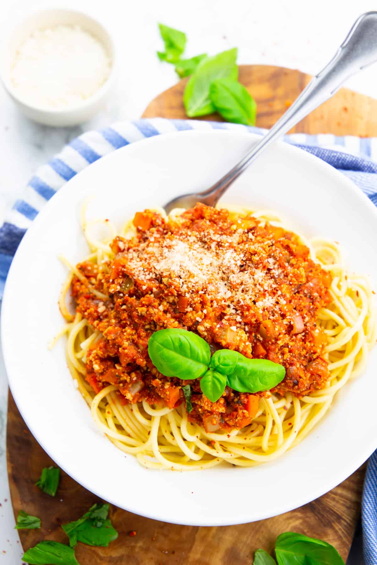 spaghetti with vegan bolognese sauce in a white bowl with a fork on a wooden board 
