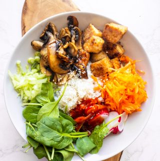 a bowl with bibimbap with tofu on a wooden board on a marble countertop
