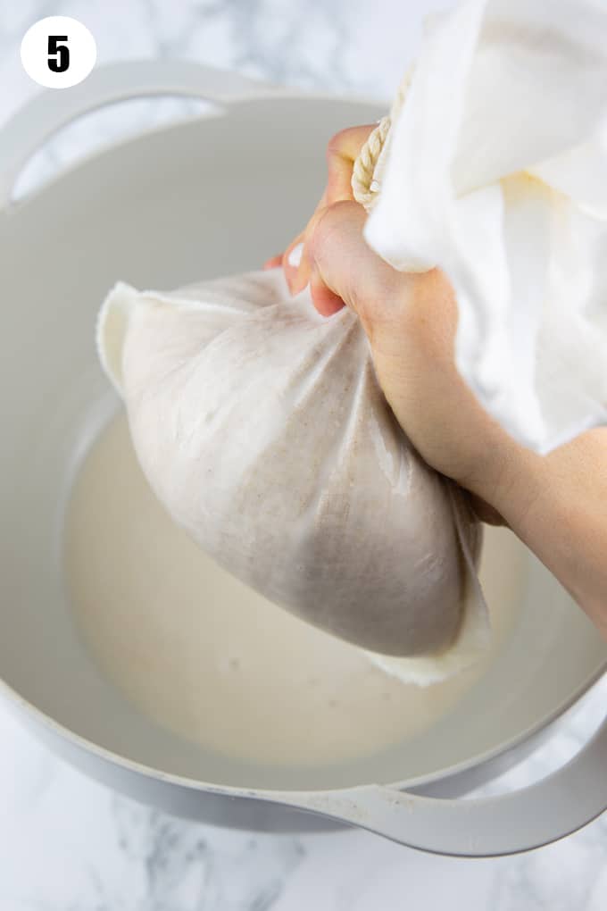 a hand holding a nut milk bag with oat milk over a bowl