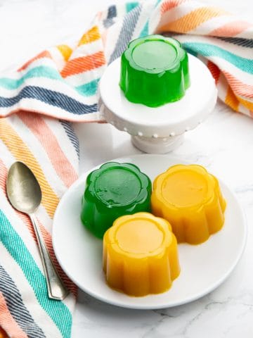 yellow and green vegan jello on a white plate and a small cupcake platter on a marble countertop