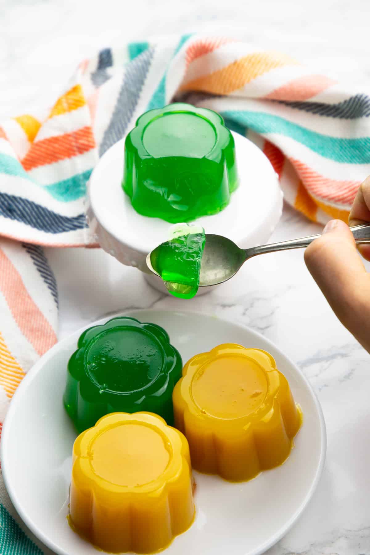 vegan jello on a white plate with a hand holding a spoon with jello 