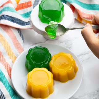 vegan jello on a white plate with a hand holding a spoon with jello