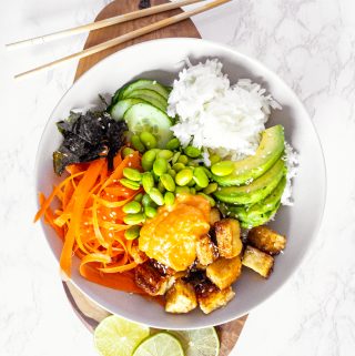 a vegan sushi bowl on a wooden cutting board with chopping sticks on the side