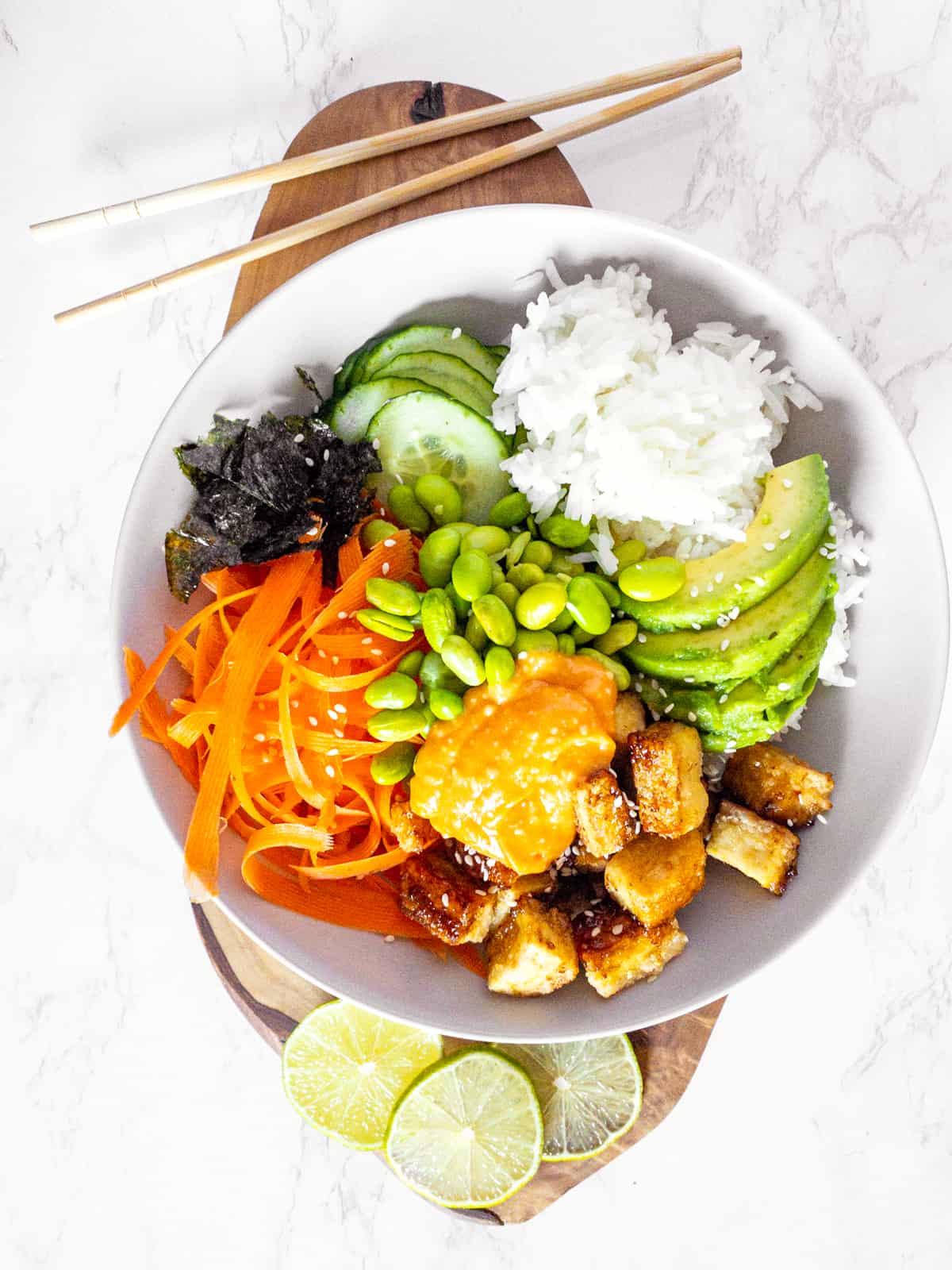 a vegan sushi bowl on a wooden cutting board with chopping sticks on the side 