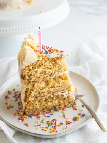 a slice of vegan birthday cake with a candle and sprinkles on a beige plate