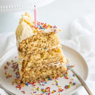 a slice of vegan birthday cake with a candle and sprinkles on a beige plate