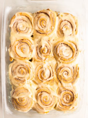 12 vegan cinnamon rolls covered with frosting in a glass dish