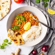 vegan dal with rice in a white bowl with a spoon on a marble countertop