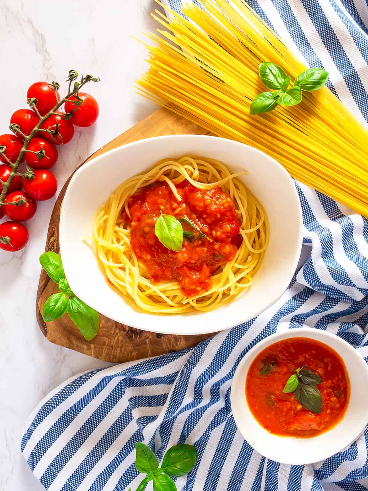 a white bowl with spaghetti with homemade tomato sauce with cherry tomatoes on a marble countertop 