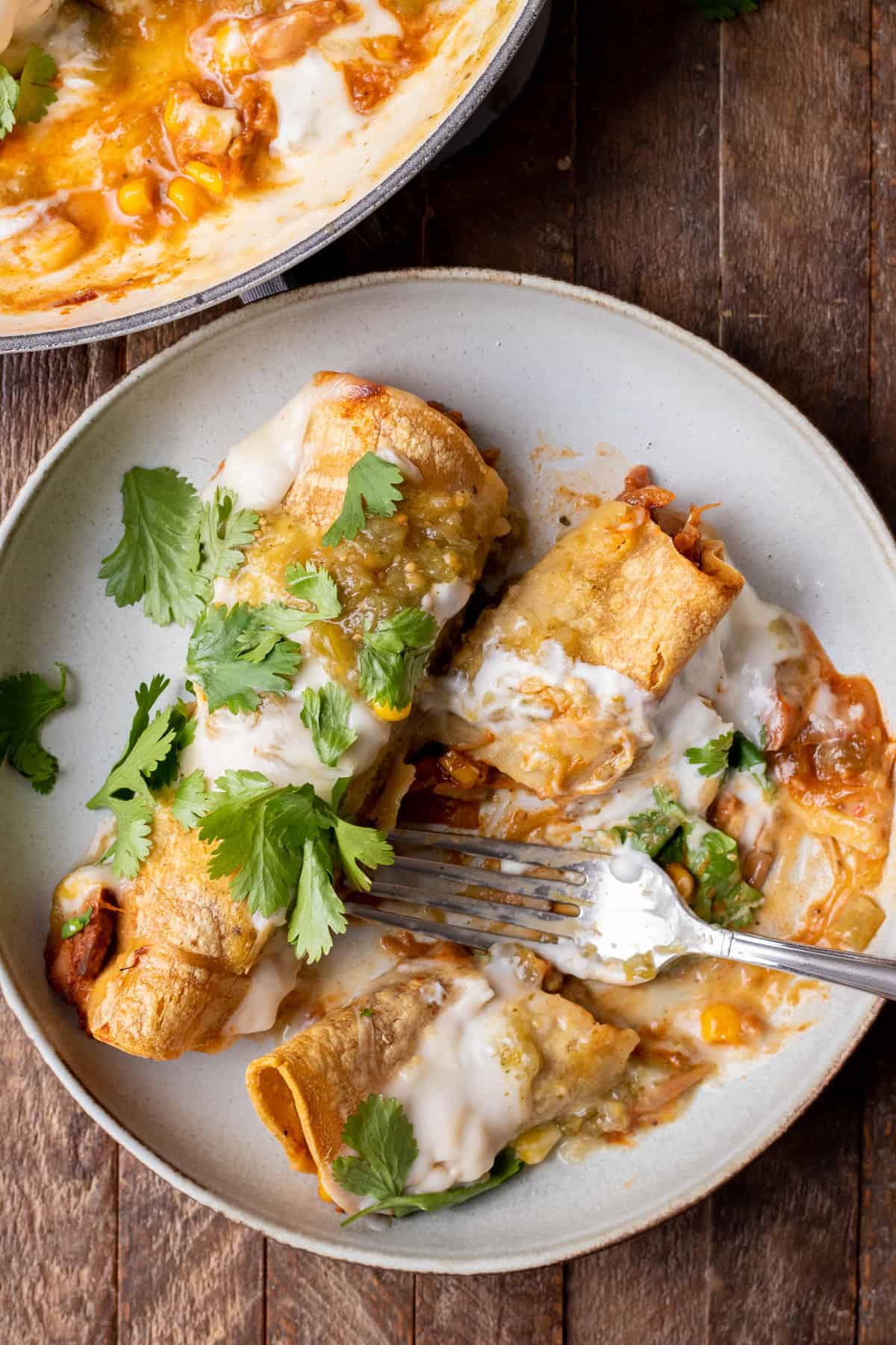 three jackfruit enchiladas on a grey plate with a fork on a wooden countertop 