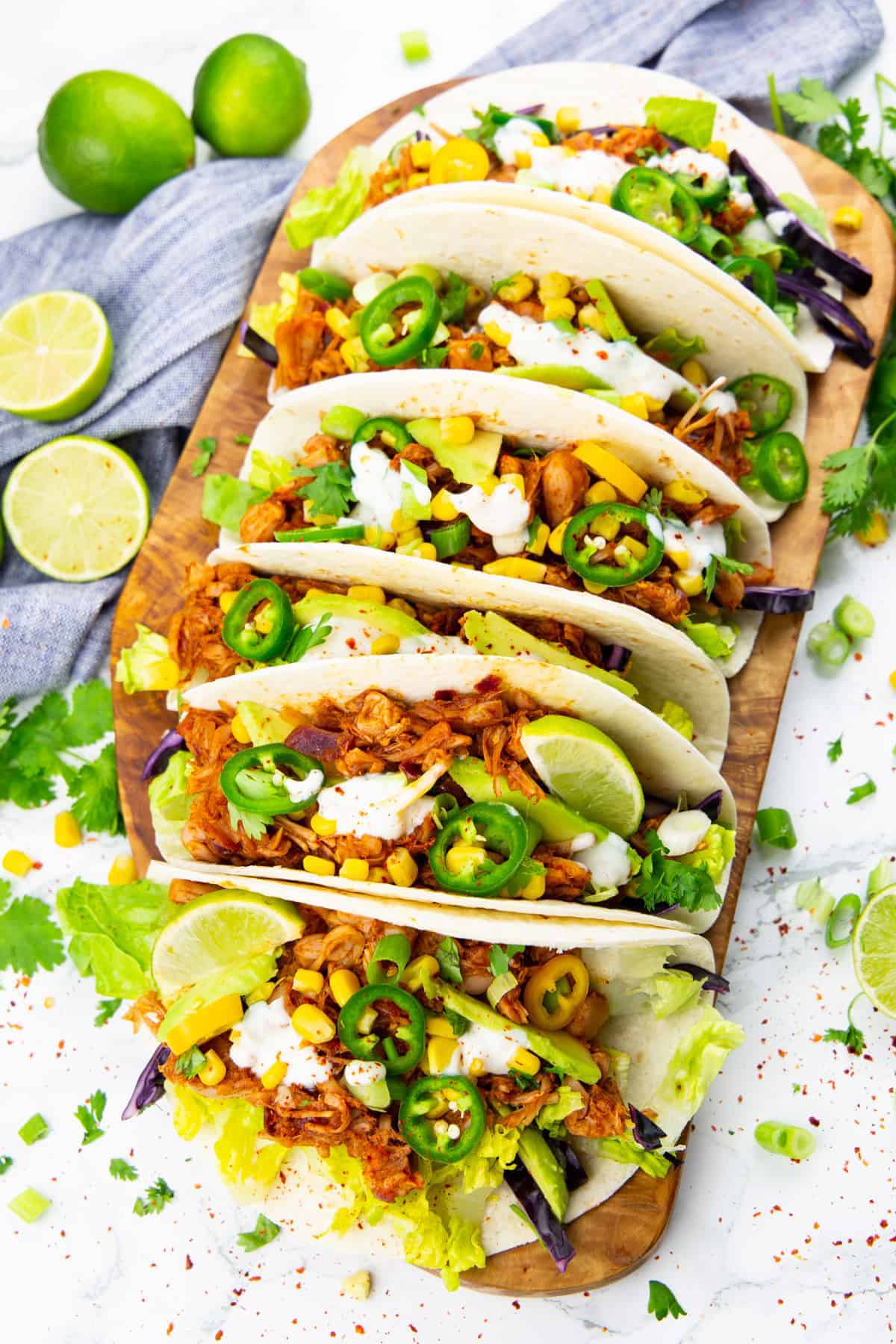 five tacos filled with jackfruit on a wooden board with limes on the side 