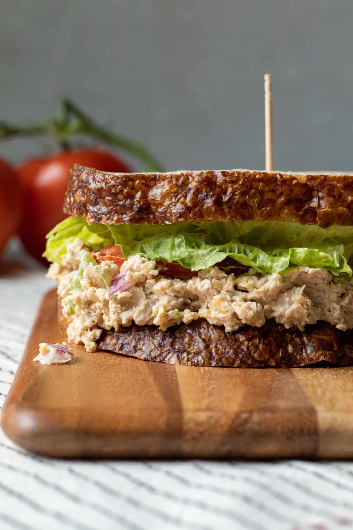 a sandwich with vegan tuna on a wooden board with tomatoes in the background