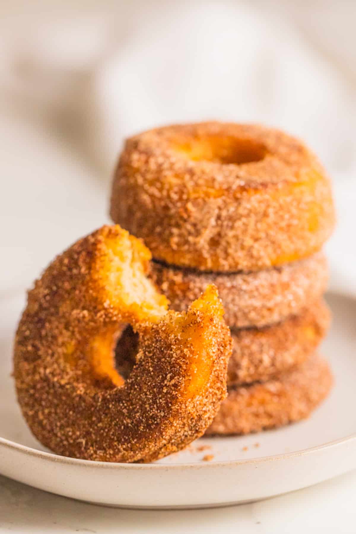 a stack of four vegan donuts with one donut with a bite missing in front 