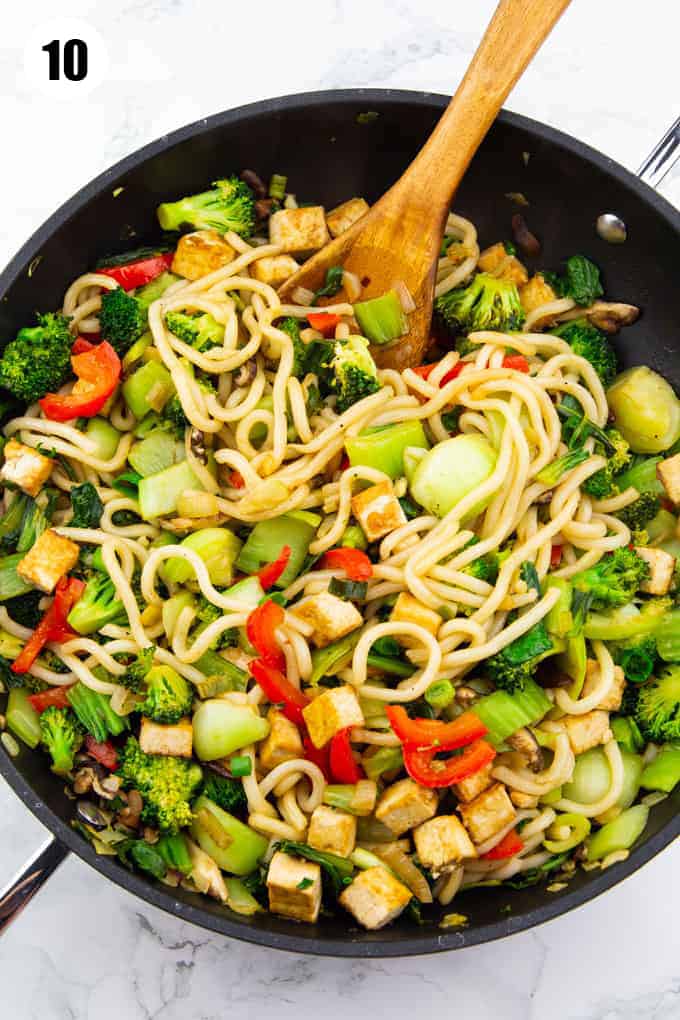 udon noodles with vegetables and tofu in a black pan