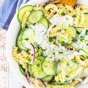 cucumber pasta salad in a white bowl with a wooden spoon