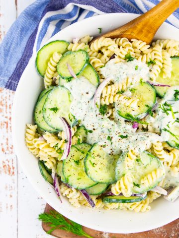 cucumber pasta salad in a white bowl with a wooden spoon