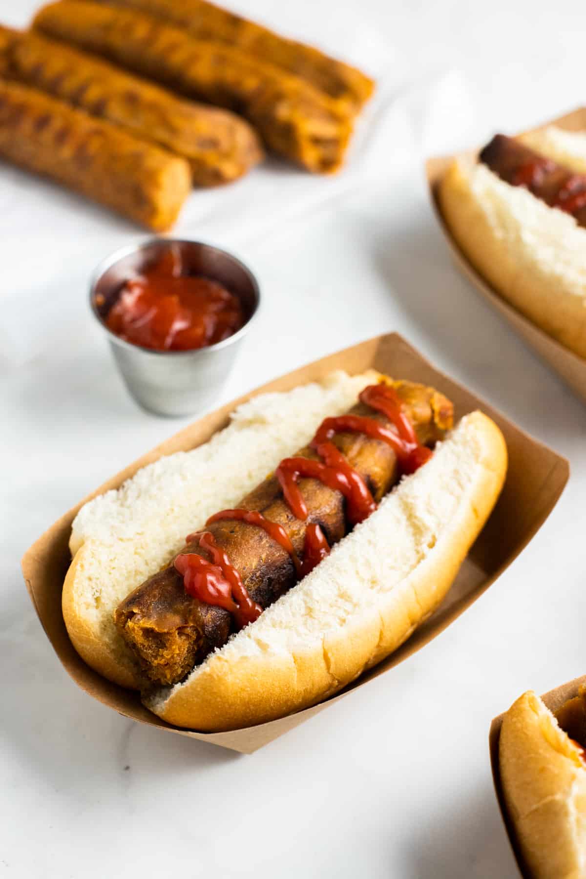 three vegan sausages in buns with ketchup on a white countertop 