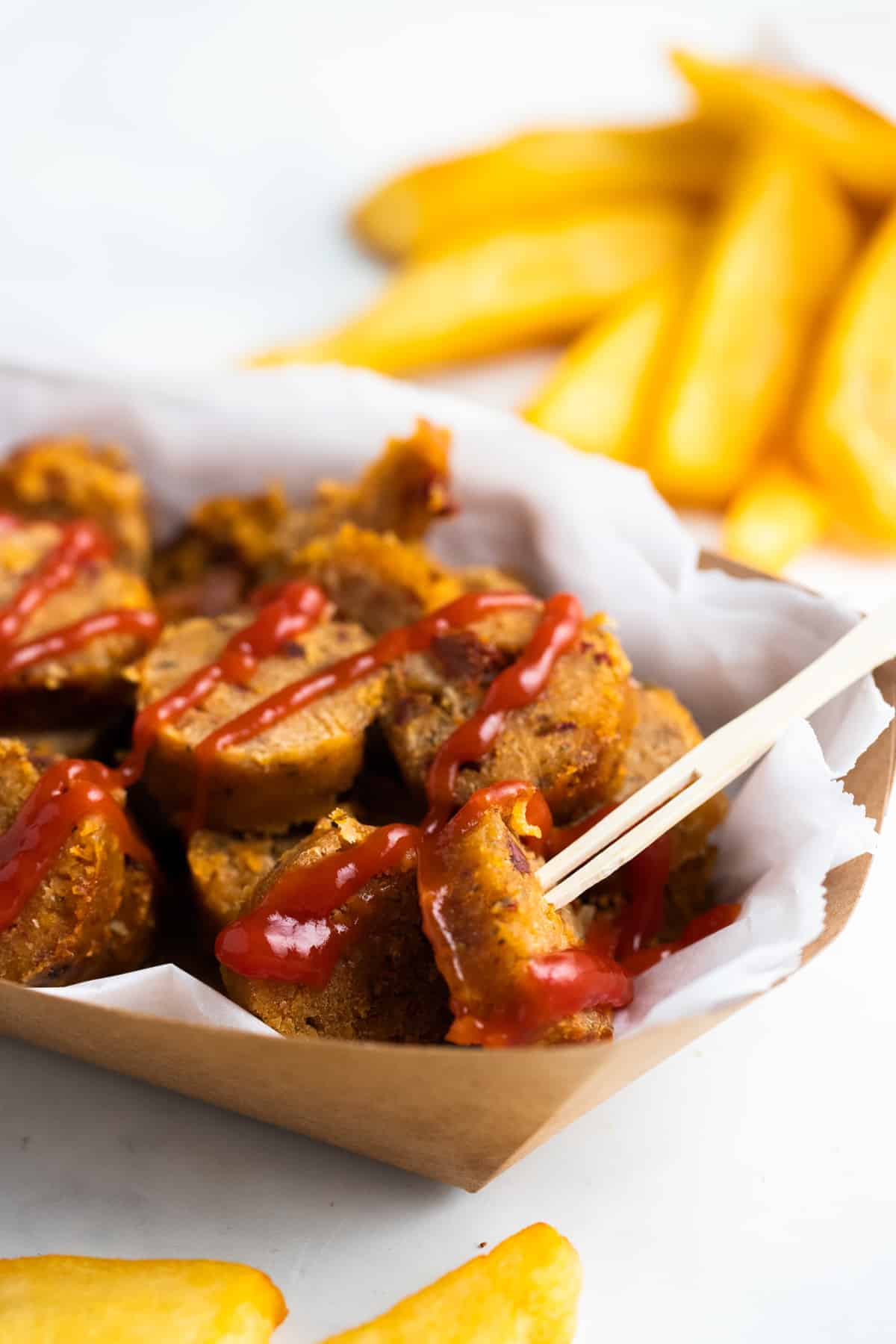 a sliced vegan sausage on a paper plate with fries in the background