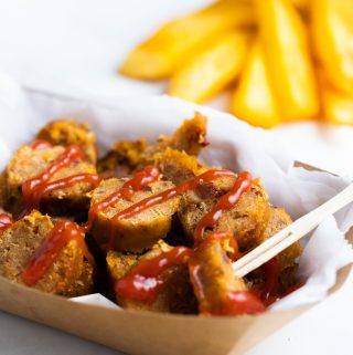 a sliced vegan sausage on a paper plate with fries in the background