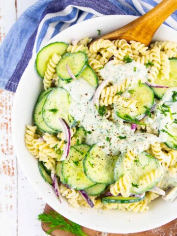 cucumber pasta salad in a white bowl with a wooden spoon