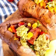 two Mexican stuffed sweet potatoes on a wooden cutting board with cherry tomatoes in the background