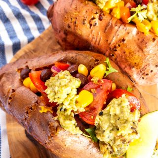 two Mexican stuffed sweet potatoes on a wooden cutting board with cherry tomatoes in the background