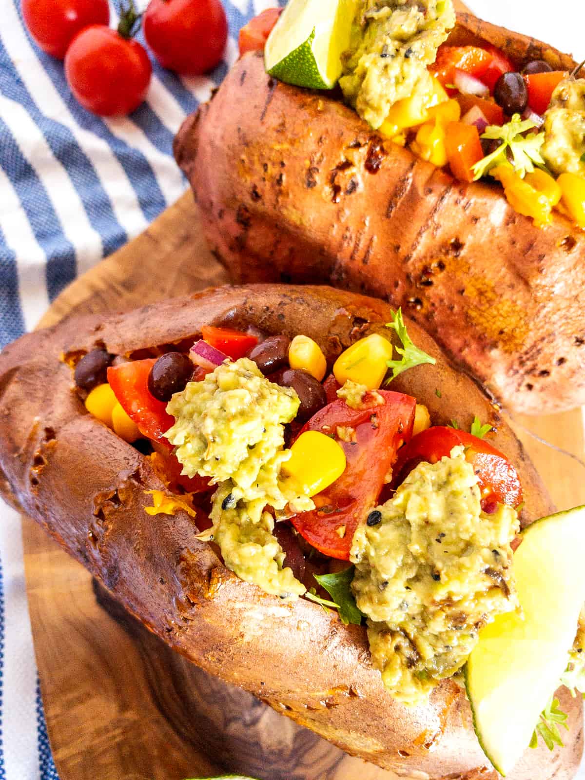 two Mexican stuffed sweet potatoes on a wooden cutting board with cherry tomatoes in the background