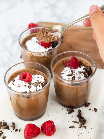 three glasses with vegan choclate mousse with a hand holding a spoon