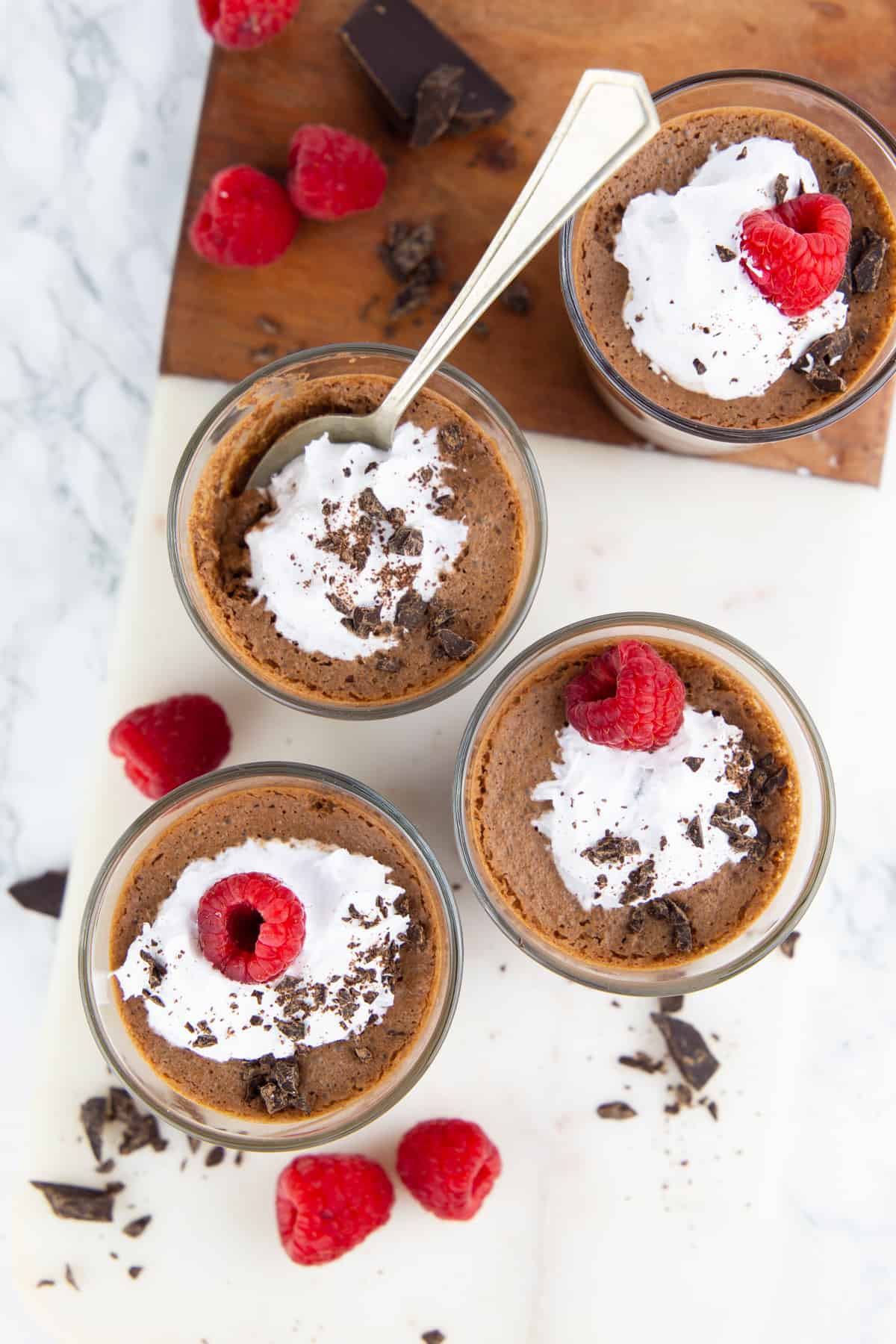 three glasses with vegan chocolate mousse decoarted with whipped cream and raspberries
