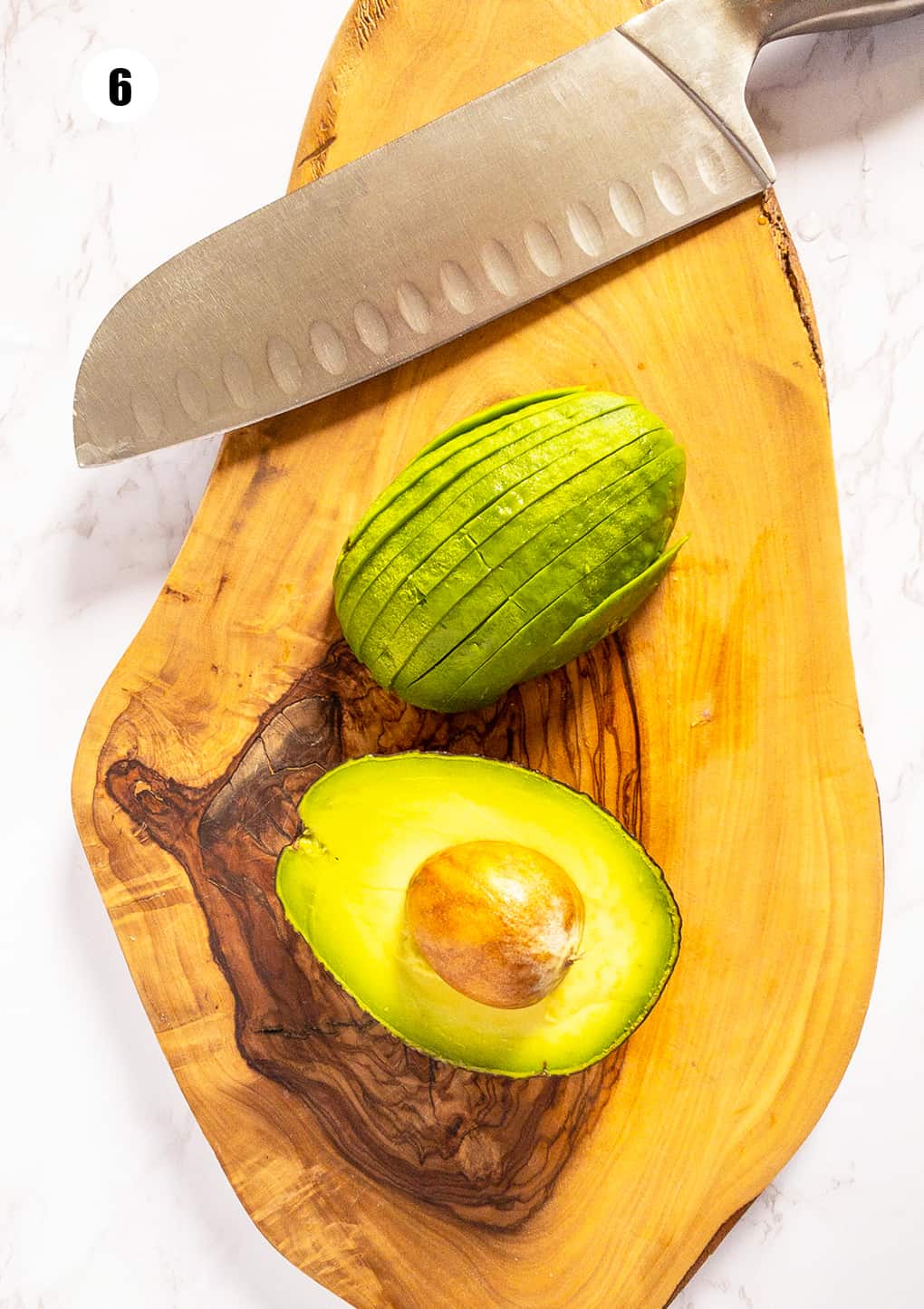 a sliced avocado with a large knife on a wooden board